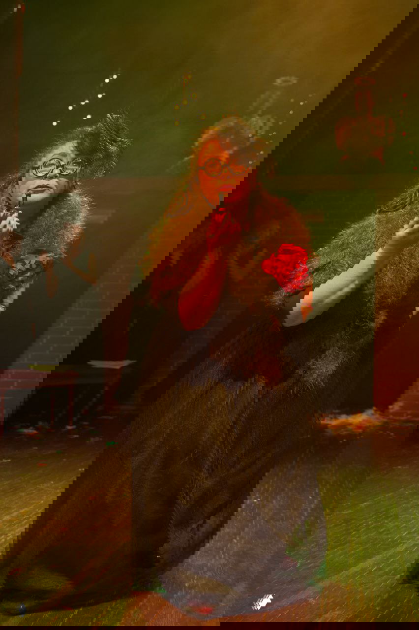 Женщина в чёрном образе и больших очках держит губную помаду на сцене, театральный реквизит и эмоциональная подача роли.