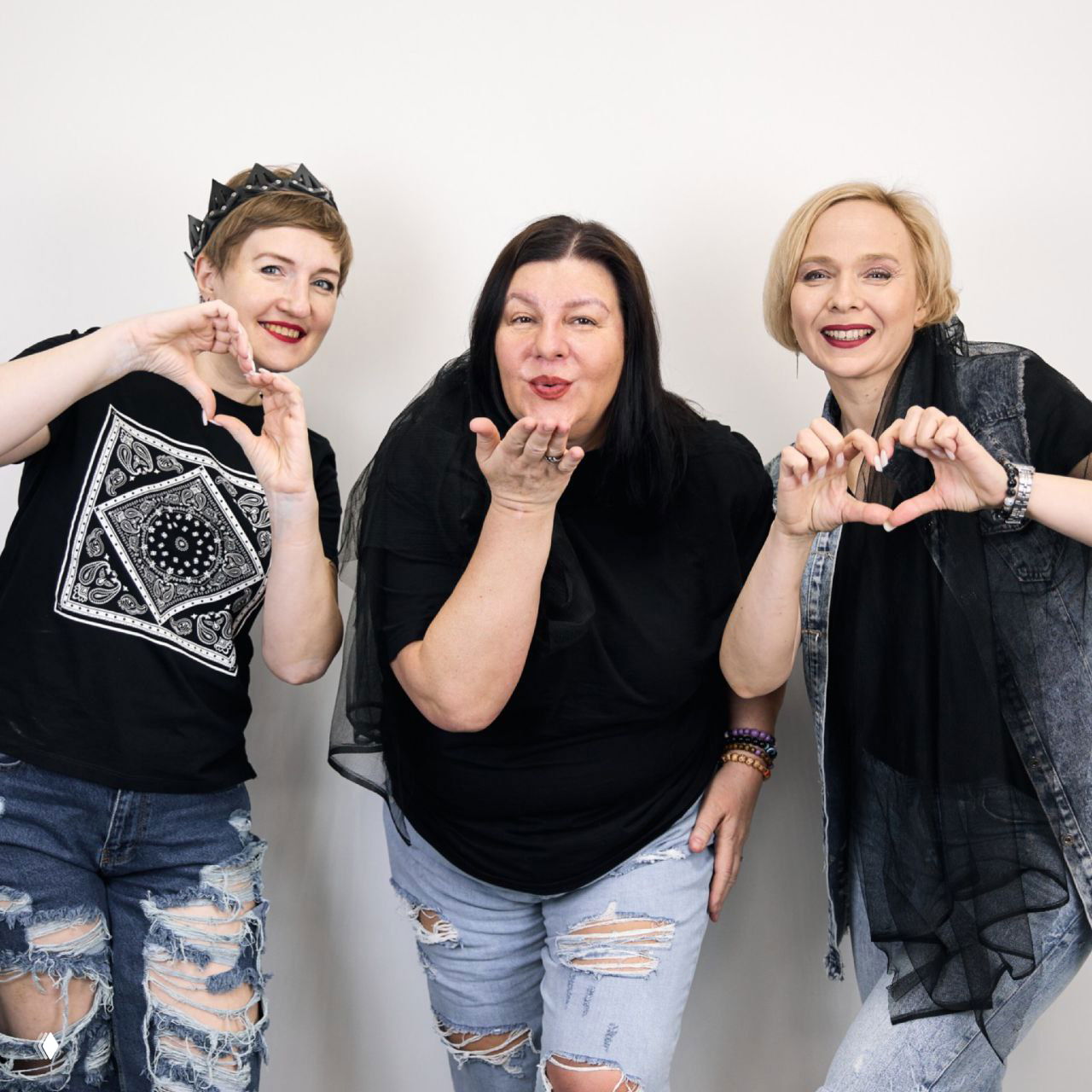 Фотография трёх улыбающихся женщин в повседневной одежде, дружеские жесты сердечками и тёплая, неформальная обстановка для анонса.