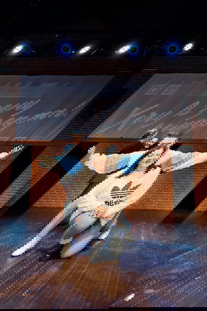 Несколько артистов в ряд на сцене под яркими софитами, фотография с обратного ракурса показывает сцену и зрительный зал.