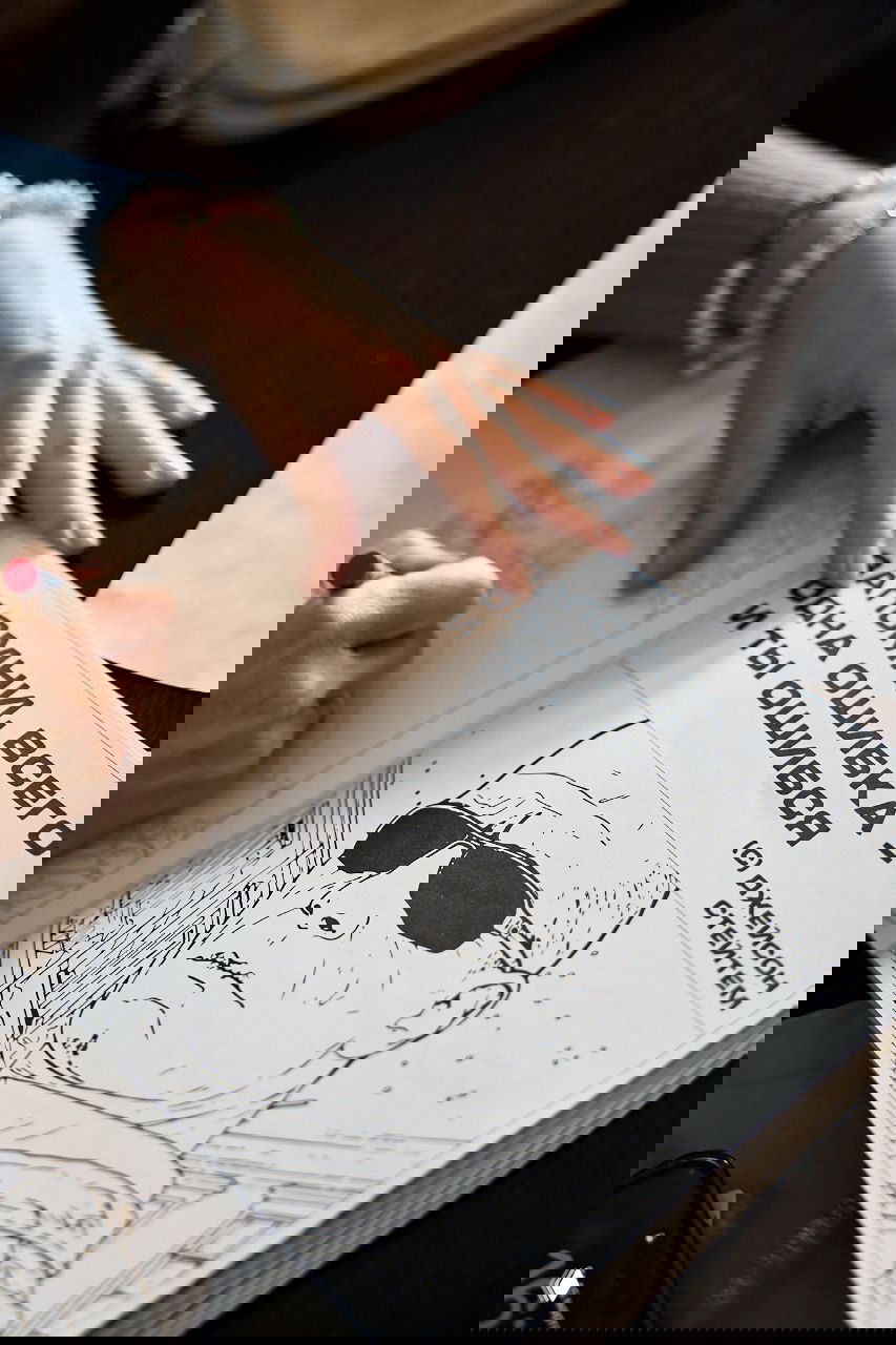 Рука рисует в раскраске/блокноте, видны страницы с иллюстрациями и подписью на русском — творческая активность в перерыве.