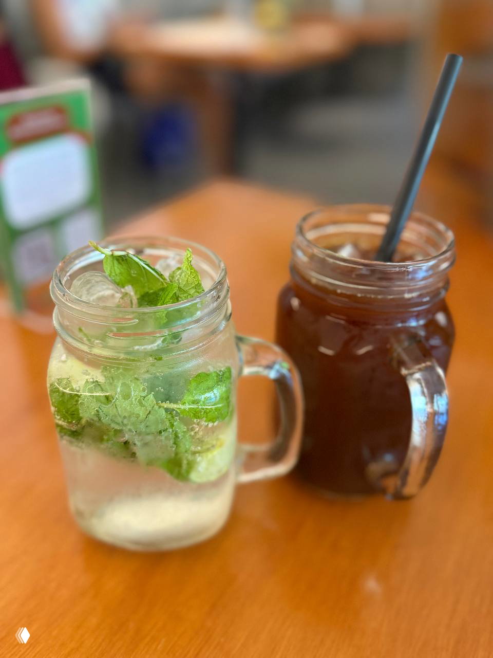Два напитка в стеклянных банках с ручкой: один с мятой и льдом (детокс), другой темного цвета с трубочкой, на деревянном столе.