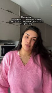 Кадр из видео: косметолог-мама в розовом свитере говорит на кухне о домашнем уходе после процедур; видно лицо и текст на экране.