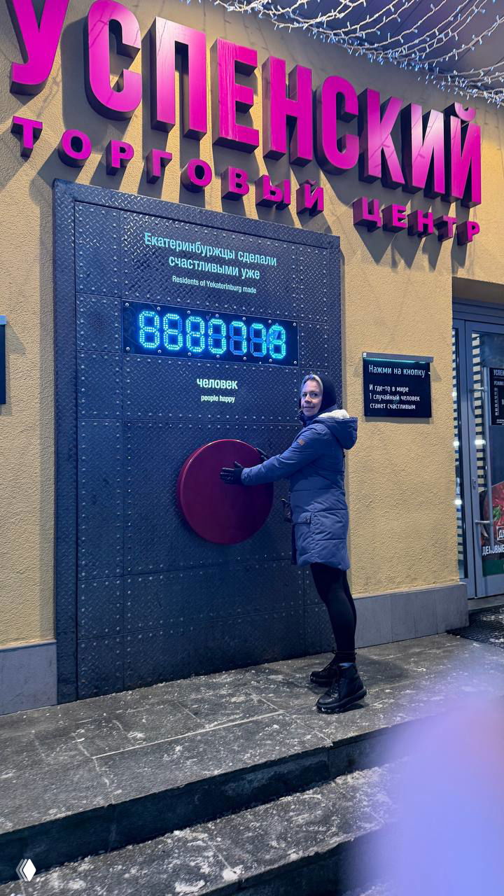 Пешеход у кнопки счастья у входа в торговый центр: яркая вывеска «Успенский» и круглая красная кнопка на стене улицы Вайнера зимой.