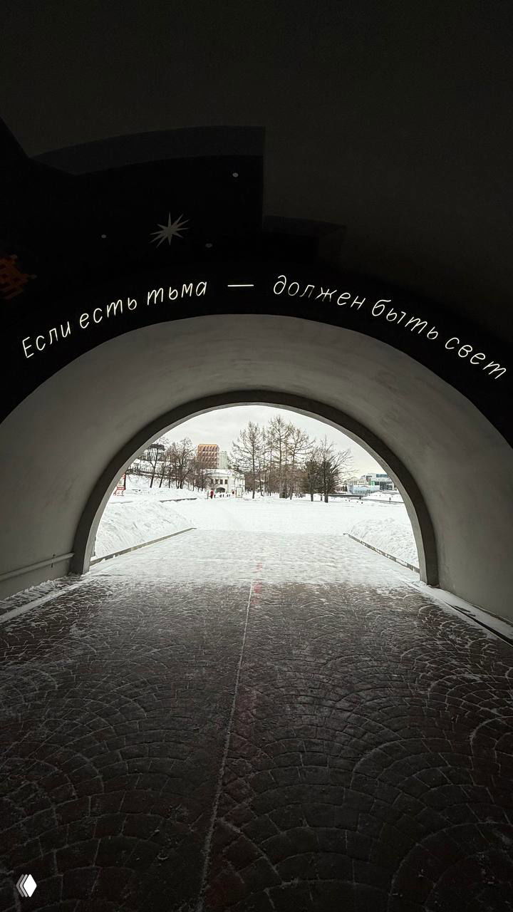 Арочный проход к парку, вид из тёмного портала на заснеженную аллею и зимний городской пейзаж под мягким светом.