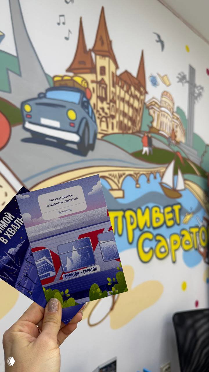Рука держит пару синих открыток на фоне настенной иллюстрации с надписью «Привет Саратов» — крупный план, яркие краски и элементы города.