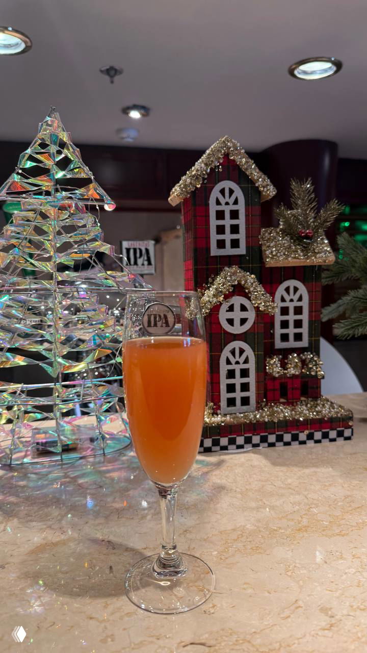 Коктейль в бокале на барной стойке на фоне праздничной декорации и миниатюрных домиков внутри салона круизного судна; уютная барная сцена.