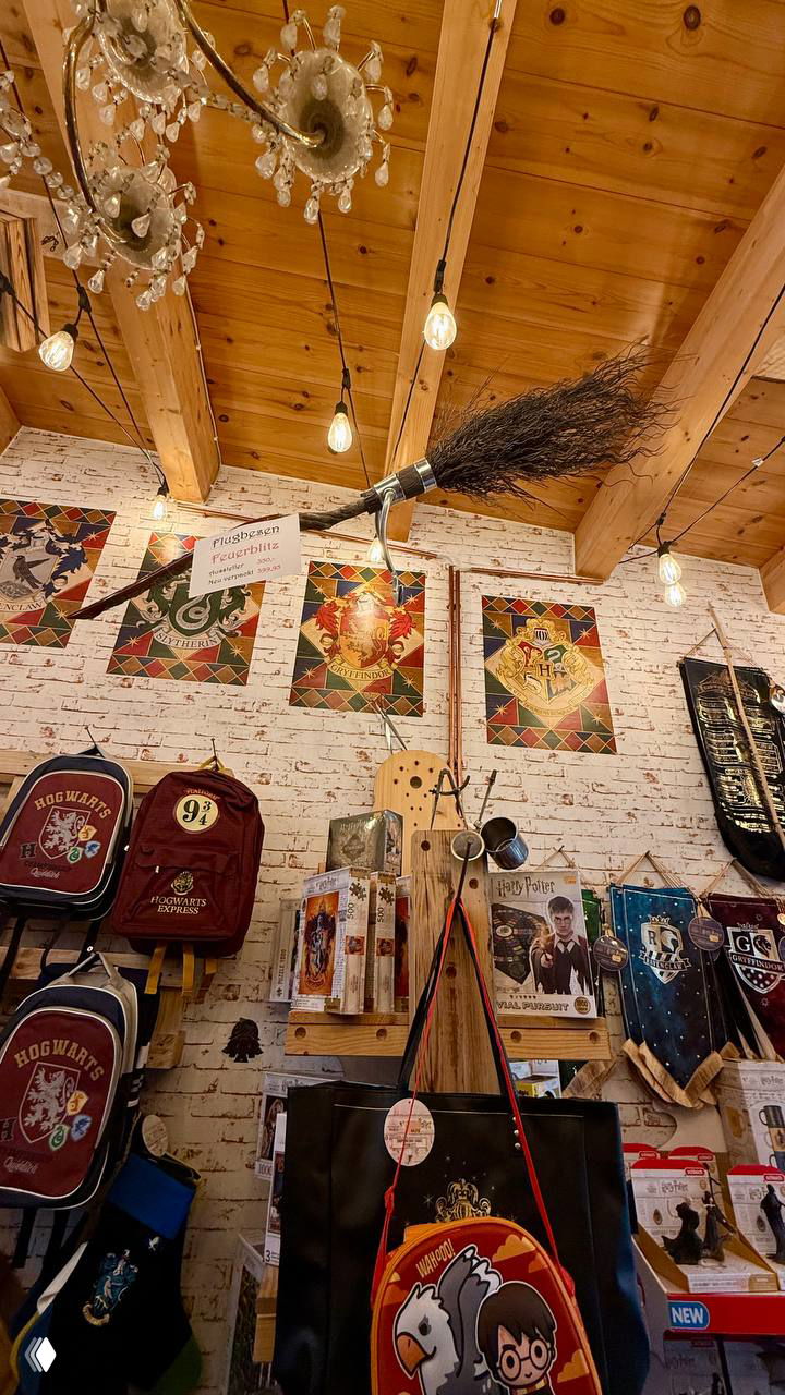 Интерьер магазина Sieben Königslande: деревянный потолок, летающая метла, постеры и рюкзаки с эмблемами Хогвартса на стенах.