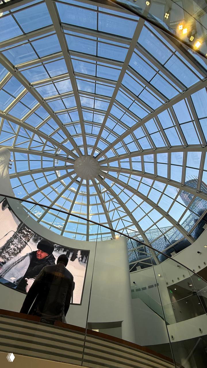 Интерьер с круглым витражным куполом в торговом центре — вид вверх на стеклянную конструкцию и экран на первом этаже.