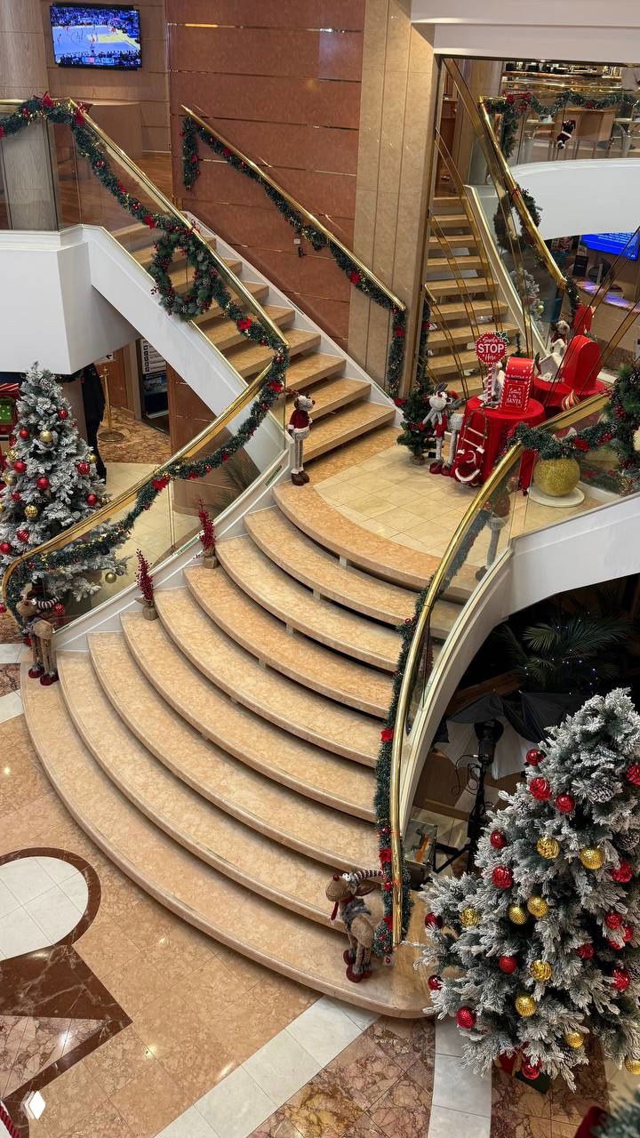 Внутри лайнера — роскошная лестница, новогоднее украшение и украшенные елки, вид на холл с декором и праздничной атмосферой.