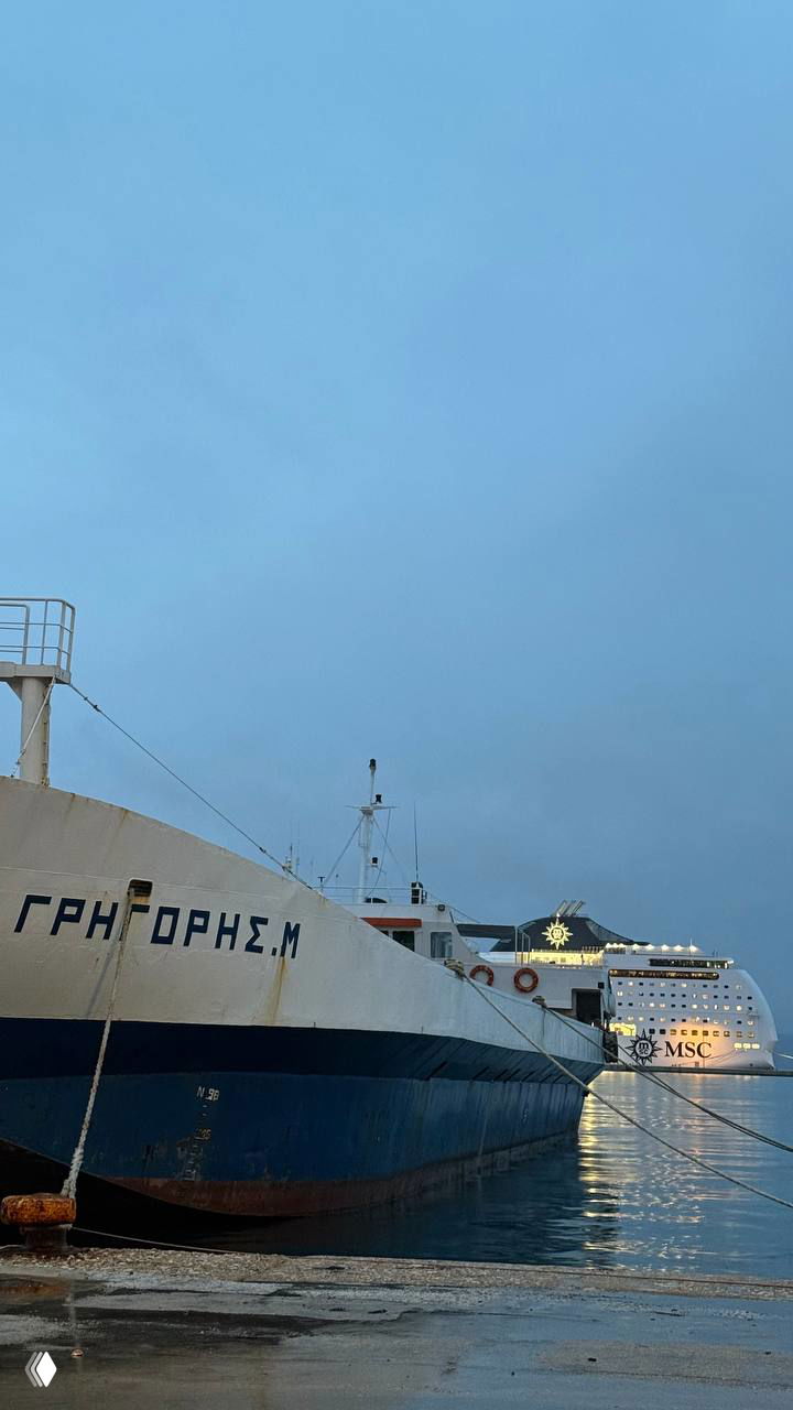 Два пришвартованных судна в гавани на сумеречном небе: на заднем плане видно подсвеченный лайнер MSC и спокойная водная гладь.