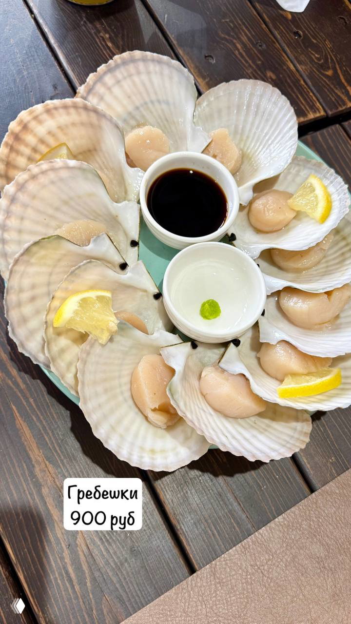 Тарелка с половинками ракушек гребешков, аккуратно выложенных вокруг соусов и ломтиками лимона, вид сверху на стол ресторана.