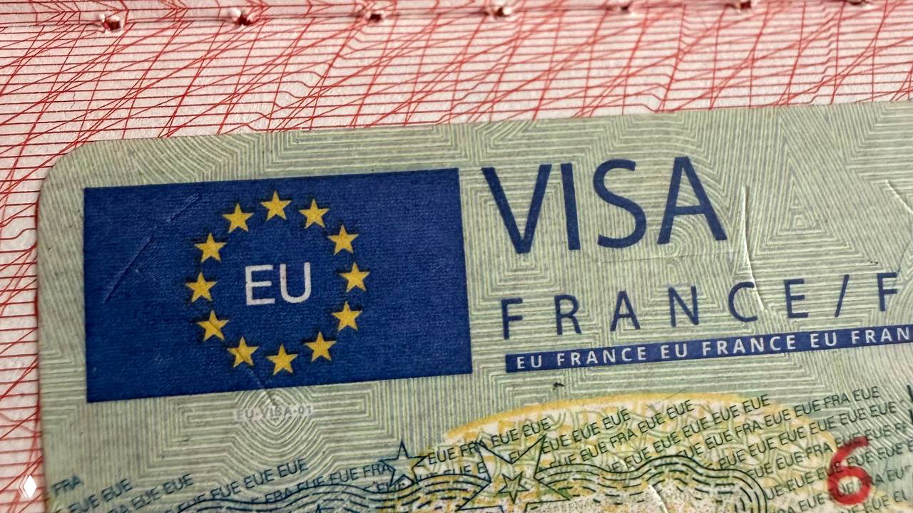 Крупный план страницы паспорта с вклеенной шенгенской визой Франции: синий прямоугольник, звезды ЕС и надпись VISA FRANCE на документе.