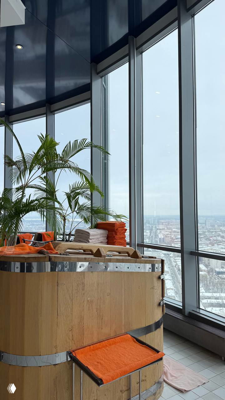 Деревянная кедровая бочка и сложенные полотенца у панорамных окон с видом на город — спа-зона внутри комплекса на верхних этажах.