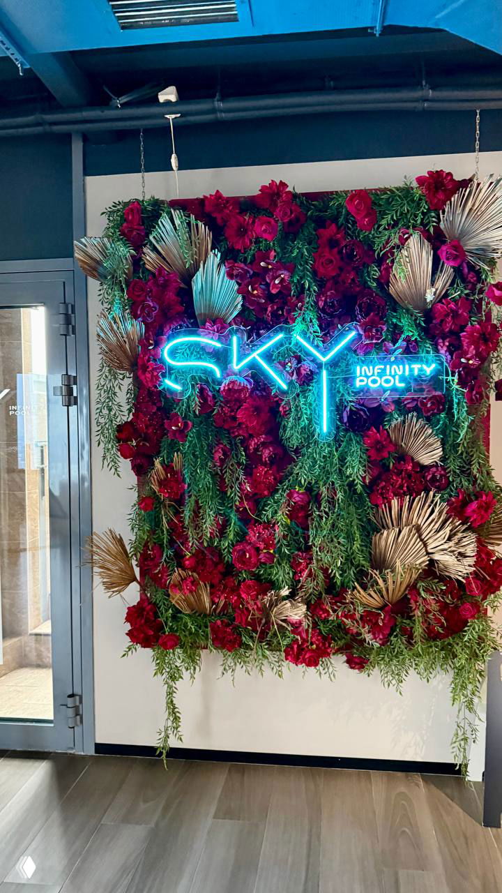 Неоновая вывеска SKY infinity pool на фоне декоративной цветочной стены у входа в бассейн на верхних этажах БЦ «Высоцкий».