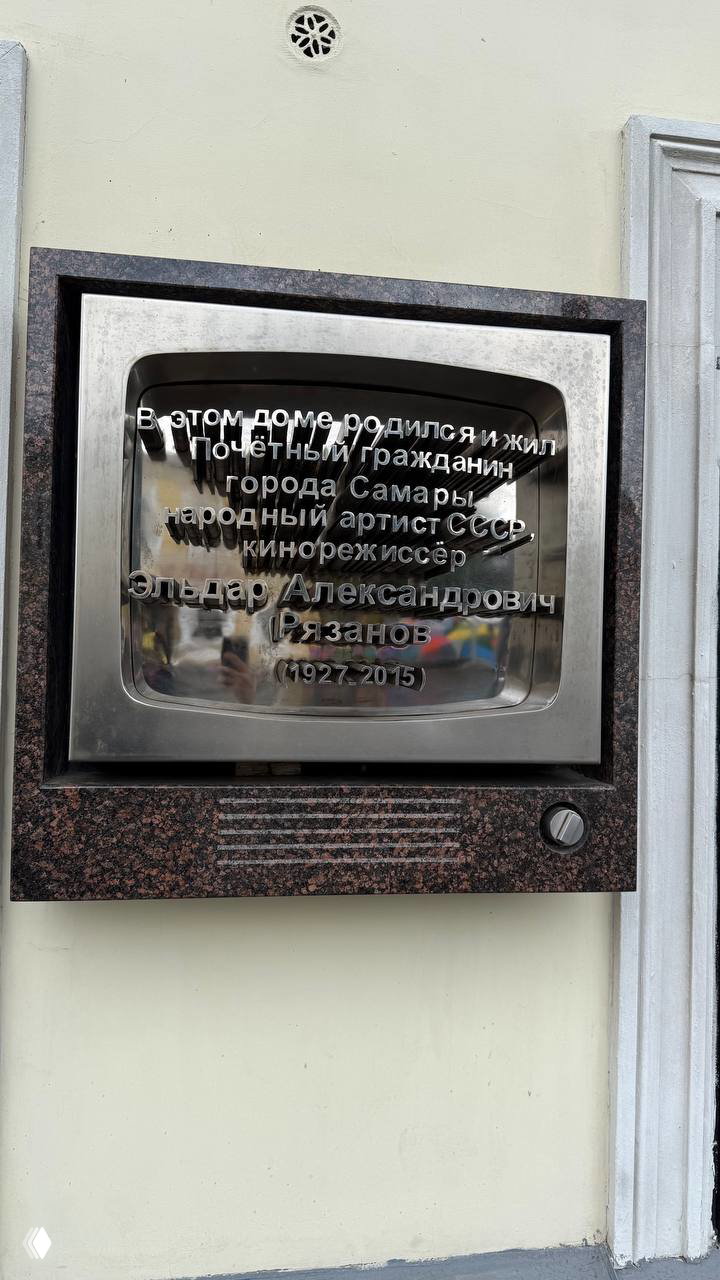 Мемориальная металлическая табличка на доме с надписью о рождении и жизни Эльдара Александровича Рязанова, отражение улицы видно в металле