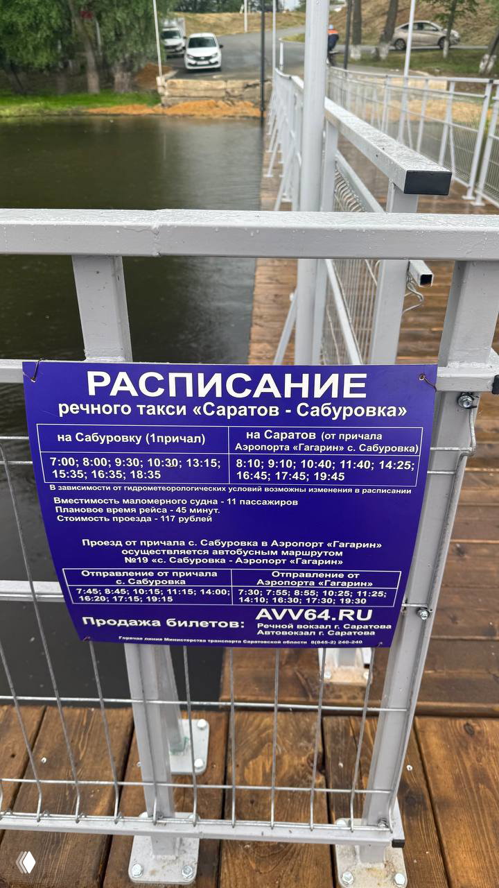 Табличка с расписанием речного такси «Саратов — Сабуровка» на металлическом ограждении причала, указаны время рейсов и стоимость билетов.