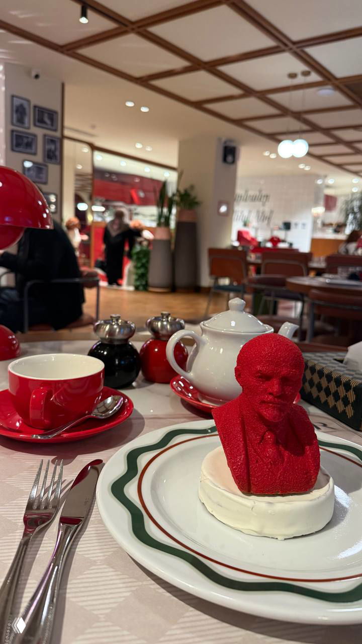 Десерт в виде красной головы Ленина на тарелке в ресторане, вокруг столовый сервиз и чашка — необычная подача и тема заведения.