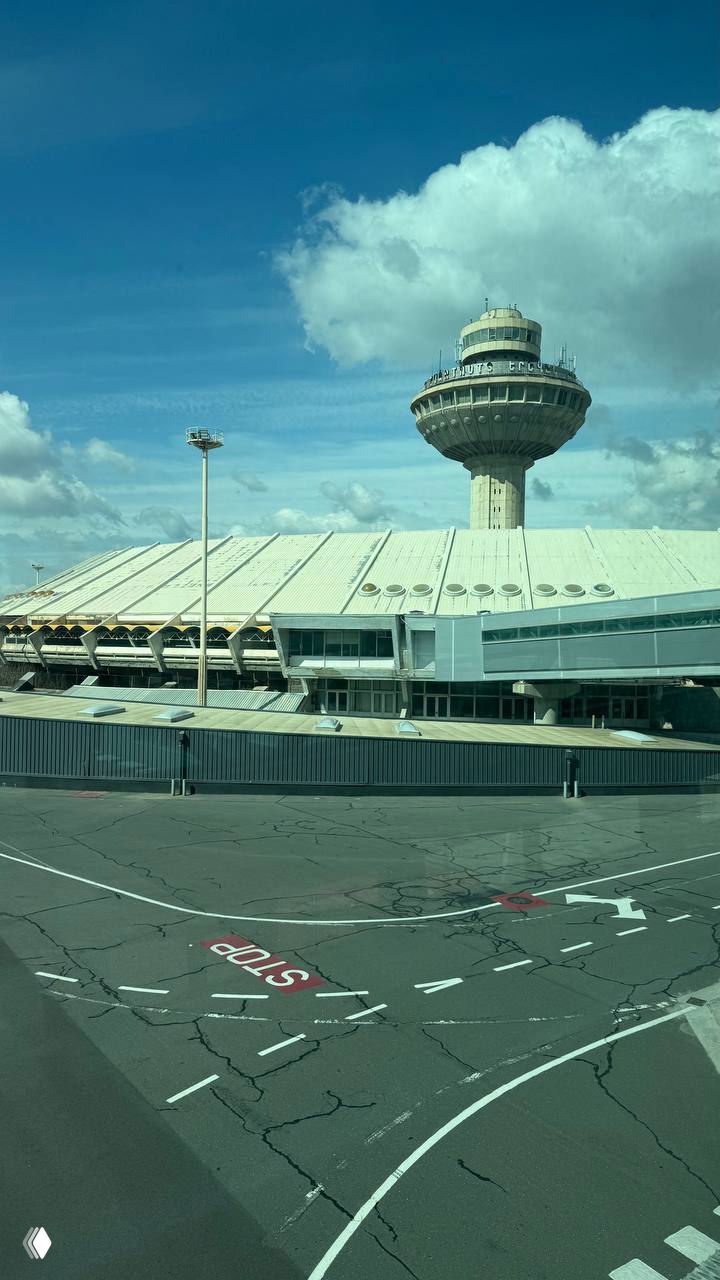 Вид на контрольно-диспетчерскую вышку и крышу терминала аэропорта Звартноц с борта самолёта: взлётно-посадочная и рулёжная зона в ясную погоду.