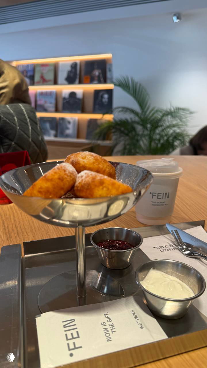 Подача сырников в креманке на металлическом подносе с соусом и стаканом с логотипом FEIN — акцент на контентной подаче блюда.