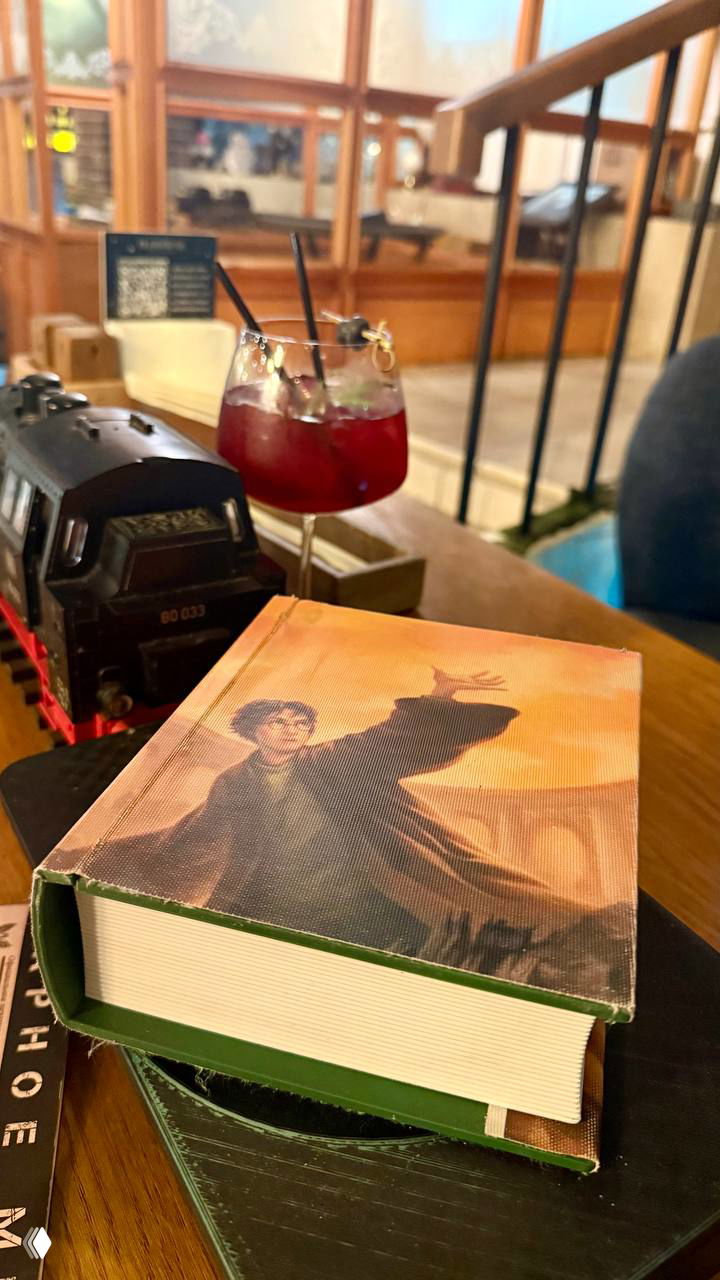 На столе миниатюрная модель поезда, книга с обложкой Гарри Поттера и яркий коктейль — подача блюд и атмосфера тематического зала.