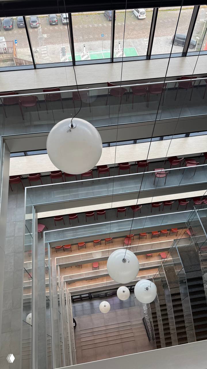 Вертикальный вид вниз на многоуровневое внутреннее пространство с балконами и панорамными окнами — холл и коридоры этажей CX Napoli Centrale.