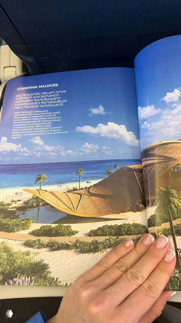 Фото разворота бортового журнала с изображением курорта на Мальдивах — пассажир держит страницу, видны яркие пляжные иллюстрации.