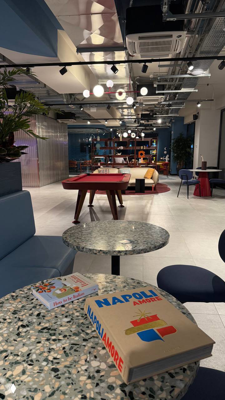 Просторный общественный зал с мягкими диванами, игровым столом и столиками — общая рабочая зона первого этажа отеля CX Napoli Centrale.