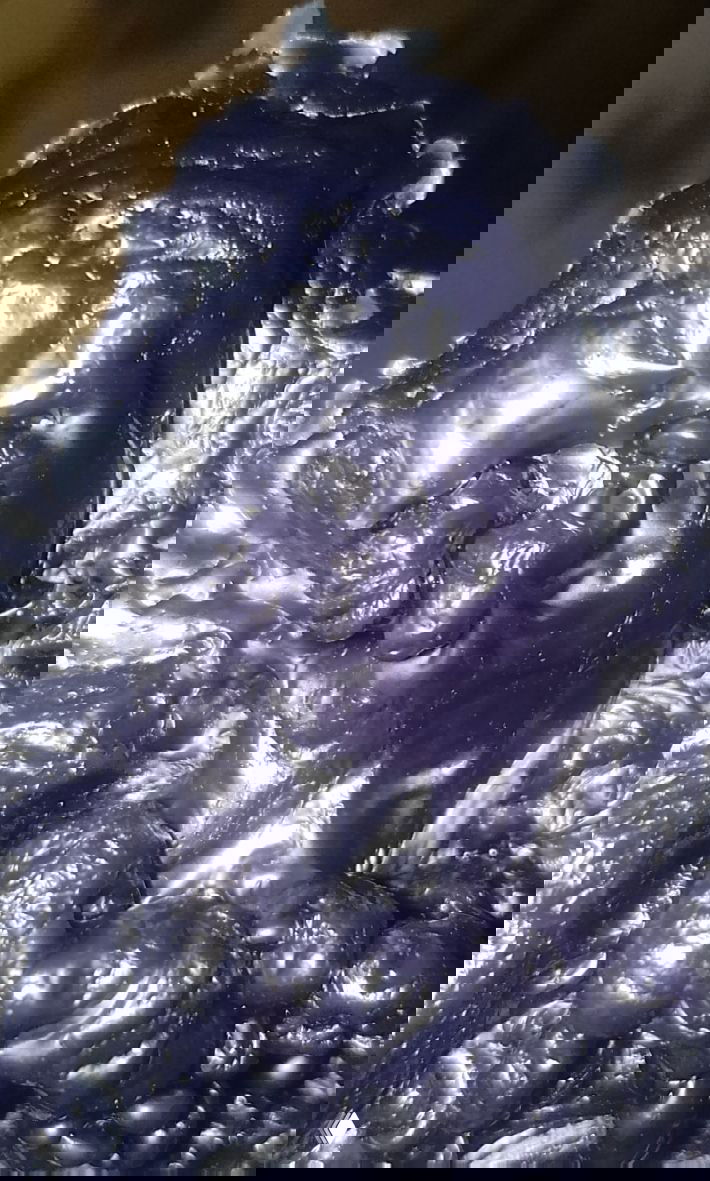 Макро-съёмка тёмно-фиолетового/чёрного воска с пузырями и узорами; поверхность с блеском и текстурой, видны складки и округлые образования.