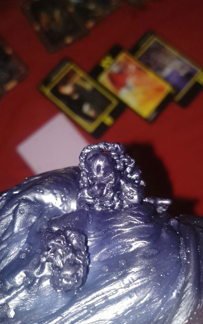 Кадр воска на фоне раскладенных карт Таро; маленькая фигурка из воска словно смотрит вперёд, видна текстура и блеск материала.