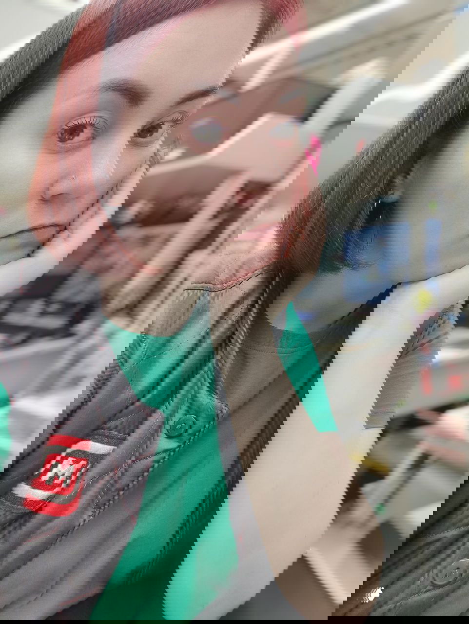 Крупный план уставшего лица сотрудницы магазина в рабочем помещении у кассы; на заднем плане видна часть рабочего пространства и техника.