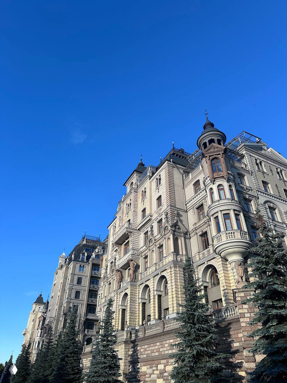 Ряд исторических зданий в классическом стиле на фоне чистого синего неба; детализированная архитектура, эркеры и фасады.