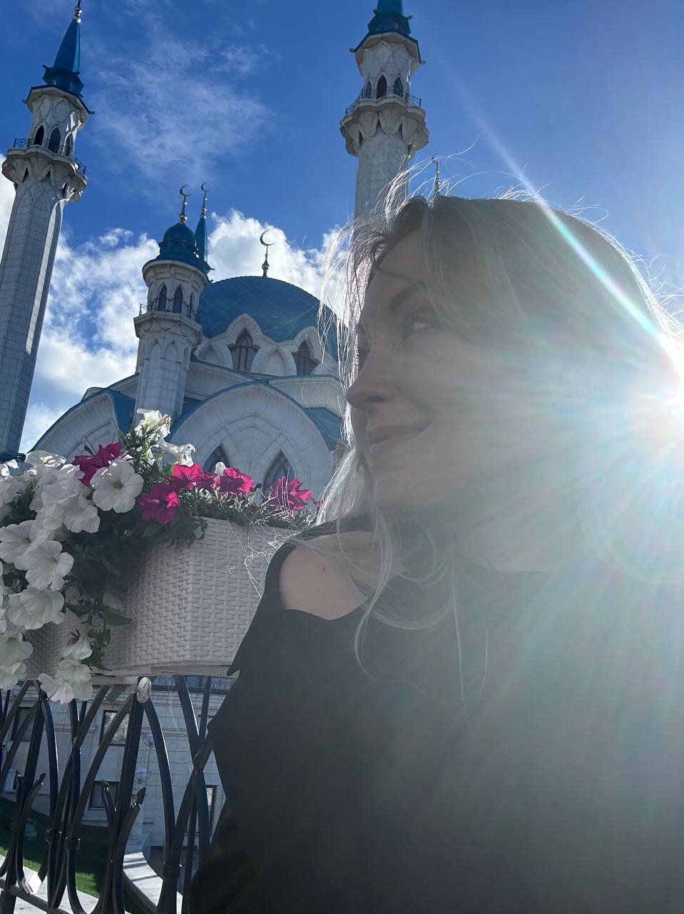 Селфи на фоне архитектуры мечети с куполами и минаретами; солнечные блики создают контровую подсветку и атмосферу вечернего света.