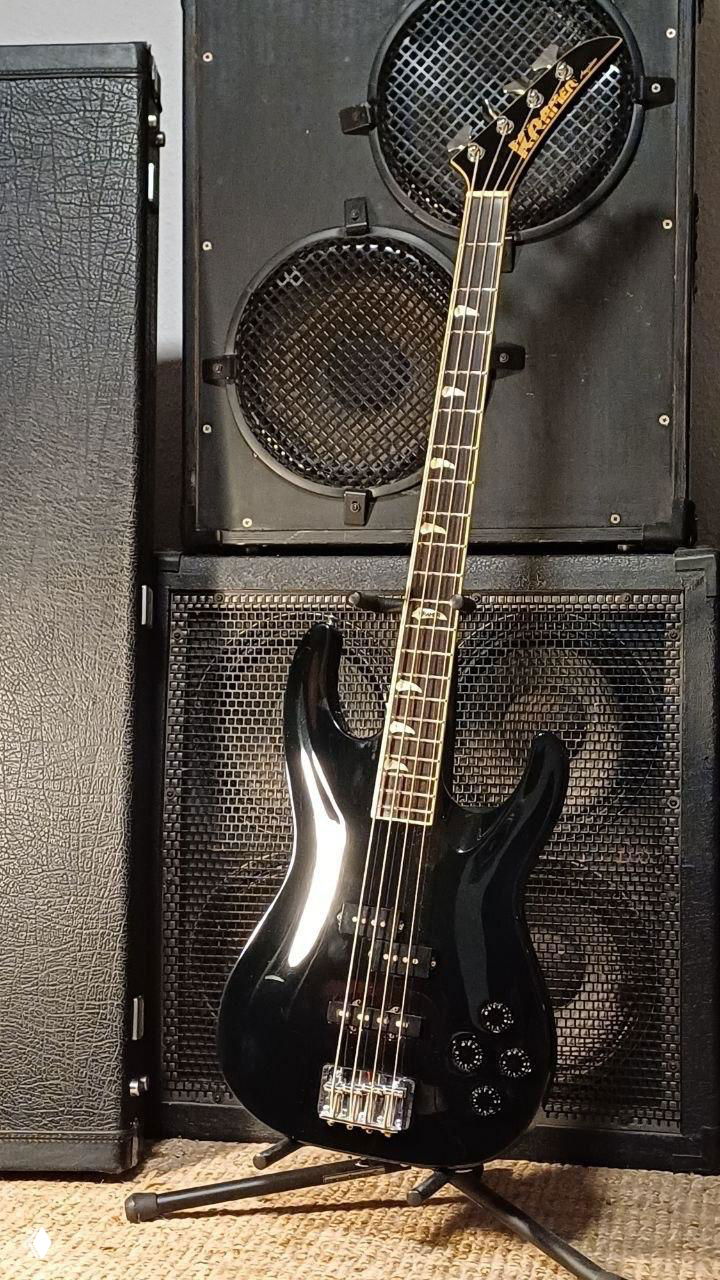 Чёрная бас-гитара Kramer на подставке на фоне кабинета и динамиков — предмет, привезённый по спецзаказу из другой страны.