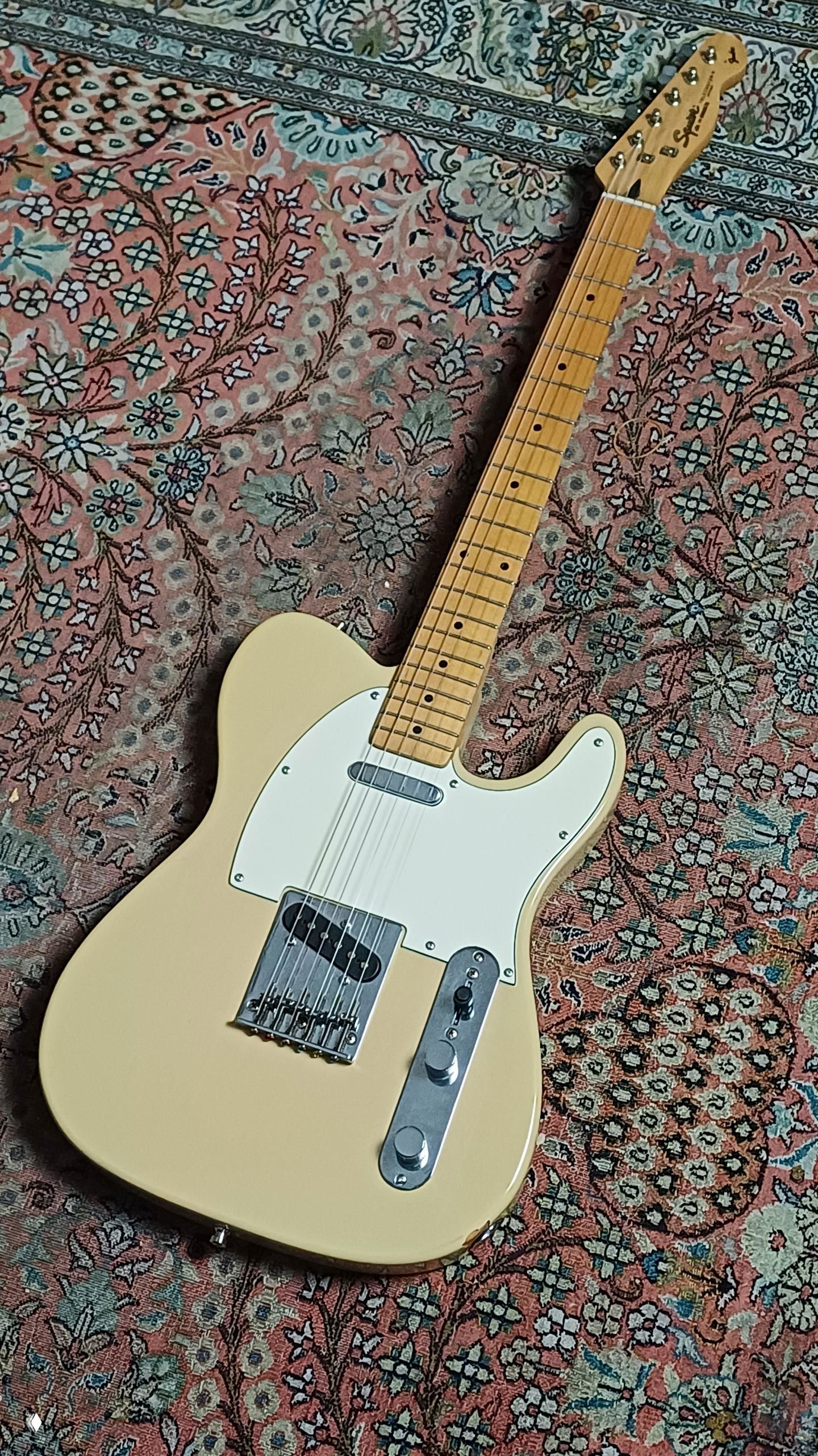 Телекастер в кремовом цвете лежит на ковре: корпус, гриф и механика в кадре, наглядно видна форма Squier Telecaster и её состояние.