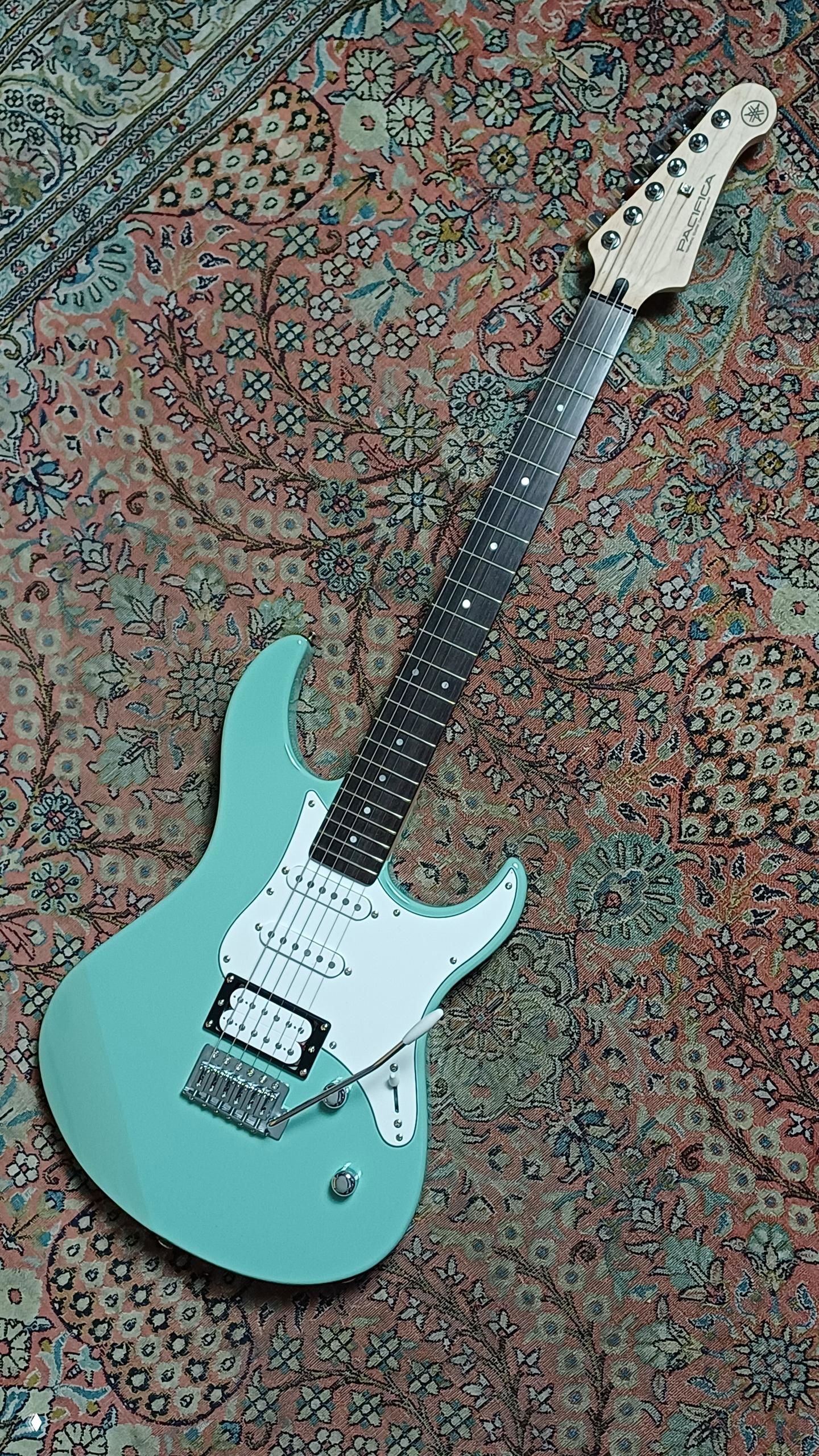 Мятная электрогитара Yamaha Pacifica на ковре, видна дека, гриф и голова грифа с логотипом — пример второй гитары из набора победителя.