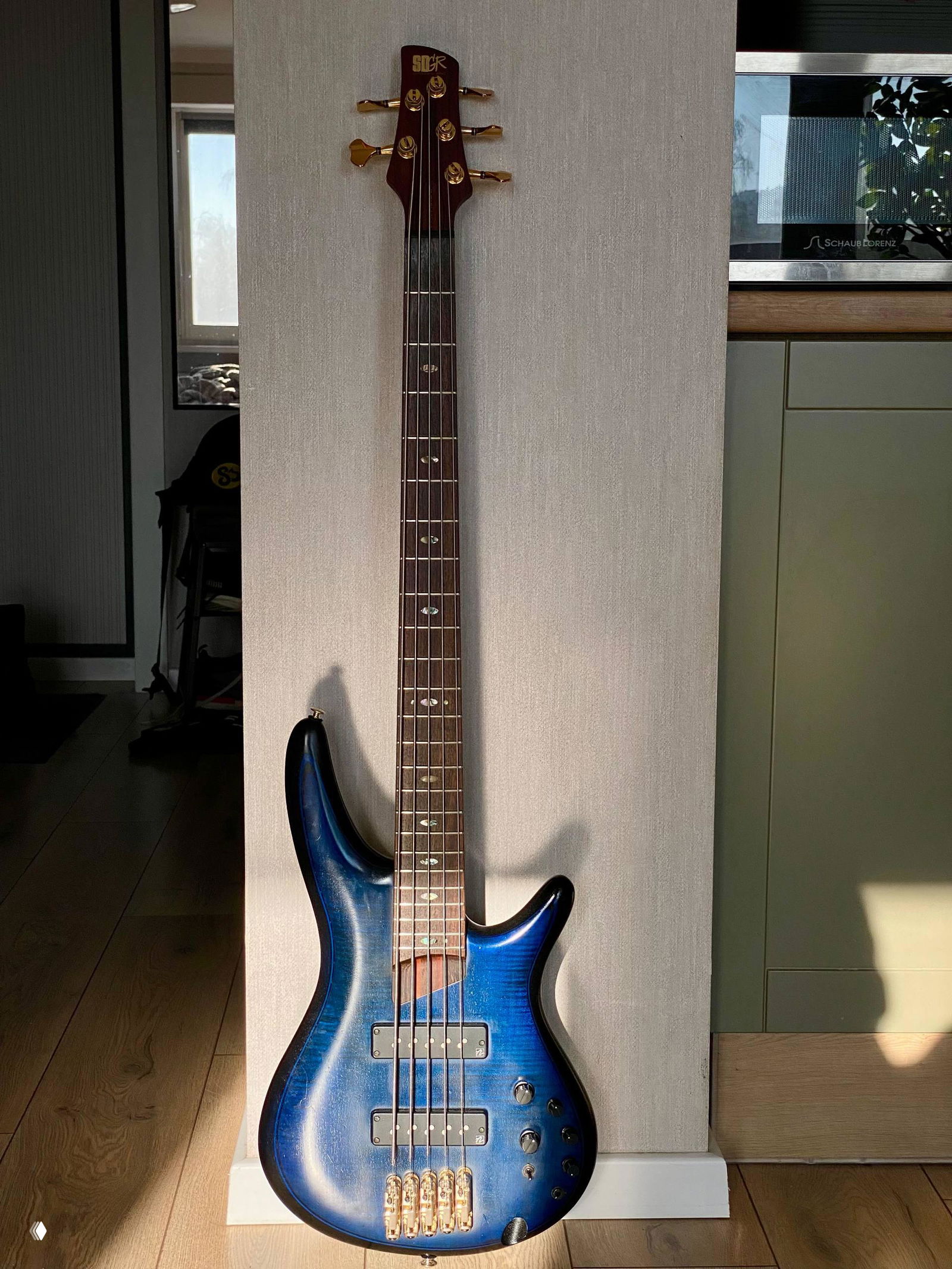 Пятиструнный бас‑гитара Ibanez SR тёмно‑синего градиента, стоит у стены на деревянном полу — фото перед упаковкой и отправкой клиенту.