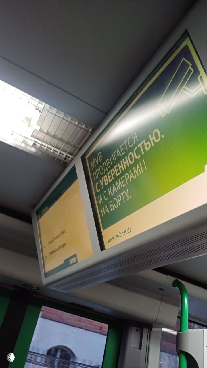 Интерьер трамвая в Германии с рекламной панелью на русском языке: зелёно-жёлтая реклама MVV над пассажирским салоном.