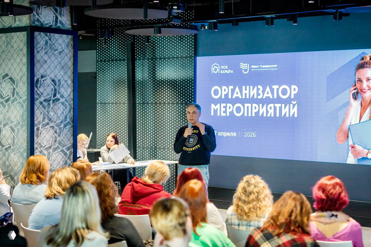 Лектор на сцене перед экраном с заголовком «Организатор мероприятий», аудитория сидит в креслах и слушает презентацию курса.