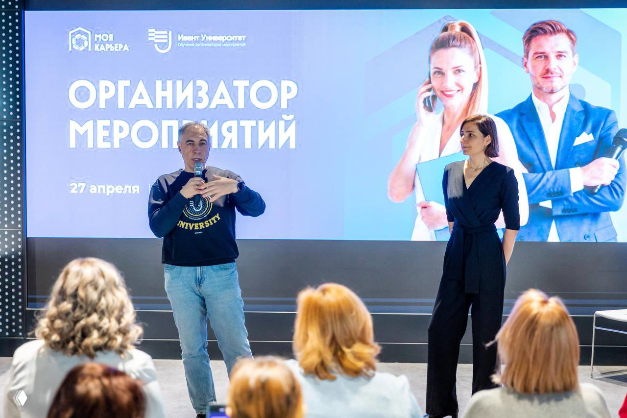 Андрей и соорганизатор на сцене рядом с экраном, на котором крупно написано «Организатор мероприятий», публичная часть церемонии.