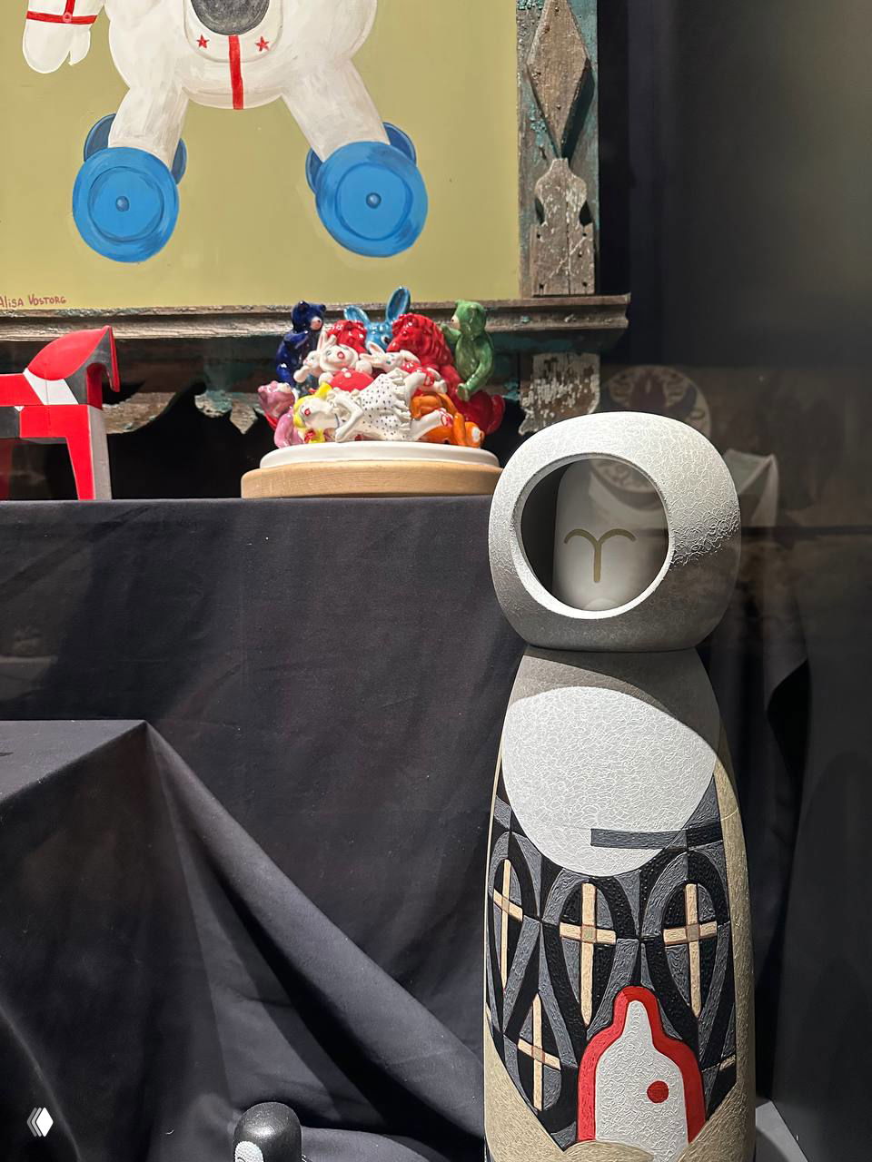 Витрина с современными керамическими и деревянными игрушками: стилизованные фигурки и минималистичные объекты на тёмном фоне экспозиции.