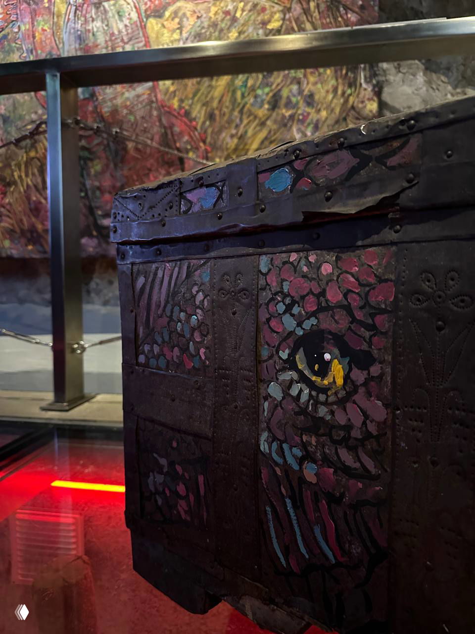 Крупный план расписанного деревянного сундучка на фоне цветной абстрактной панели — экспонат, демонстрирующий народные мотивы в современном ключе.