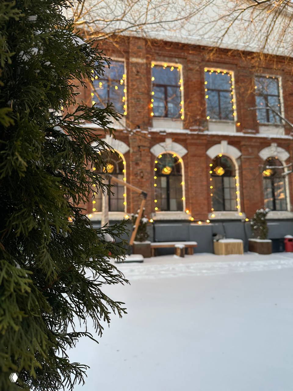 Уютный двор лофта с гирляндами и снежным покрывалом, кирпичный фасад и подсвеченные окна — внешний вид площадки форума CSTB.PRO.MEDIA.