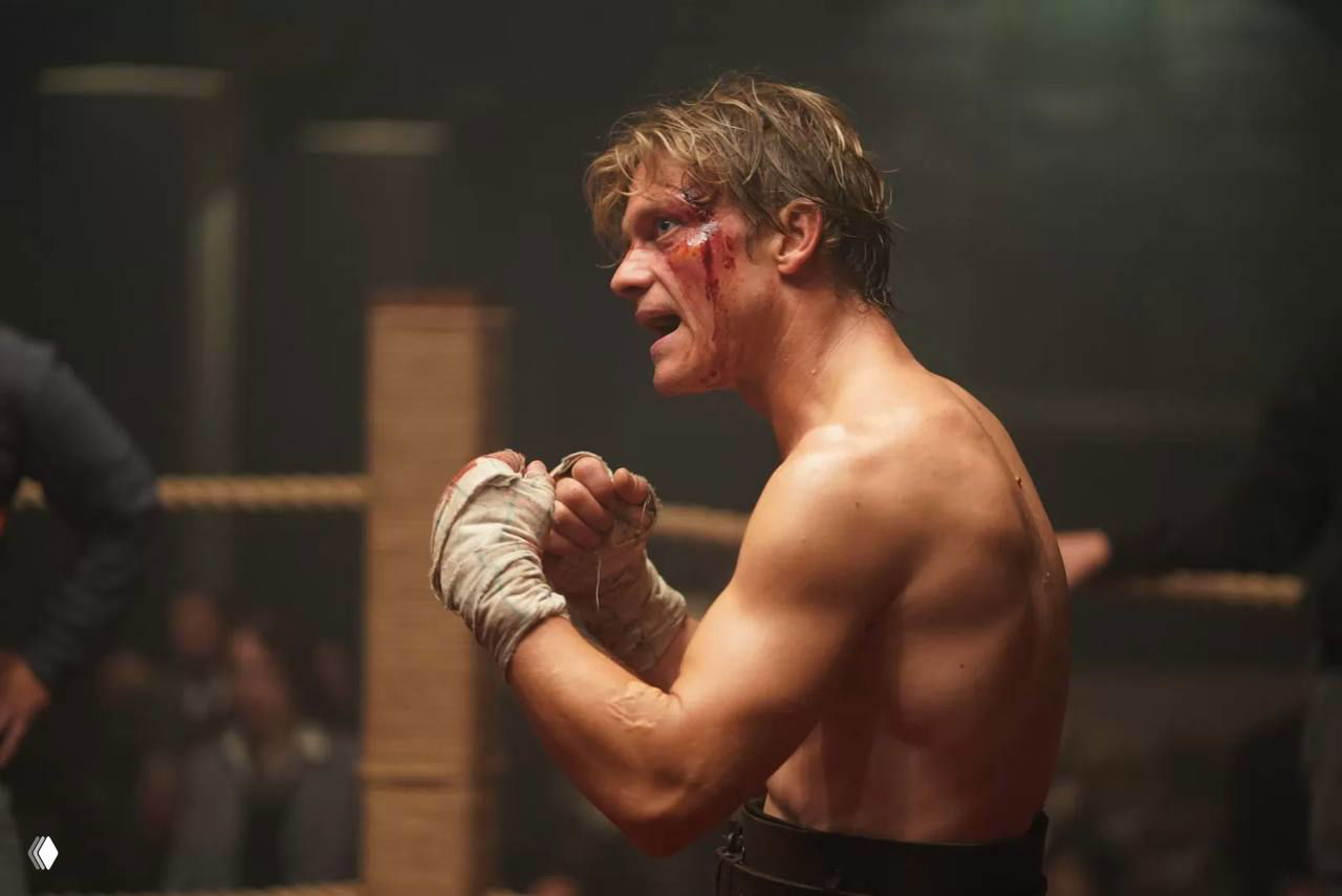 Кадр из кулачного боя: боец с забинтованными руками и кровью на лице стоит в ринге, видна напряженная сцена поединка