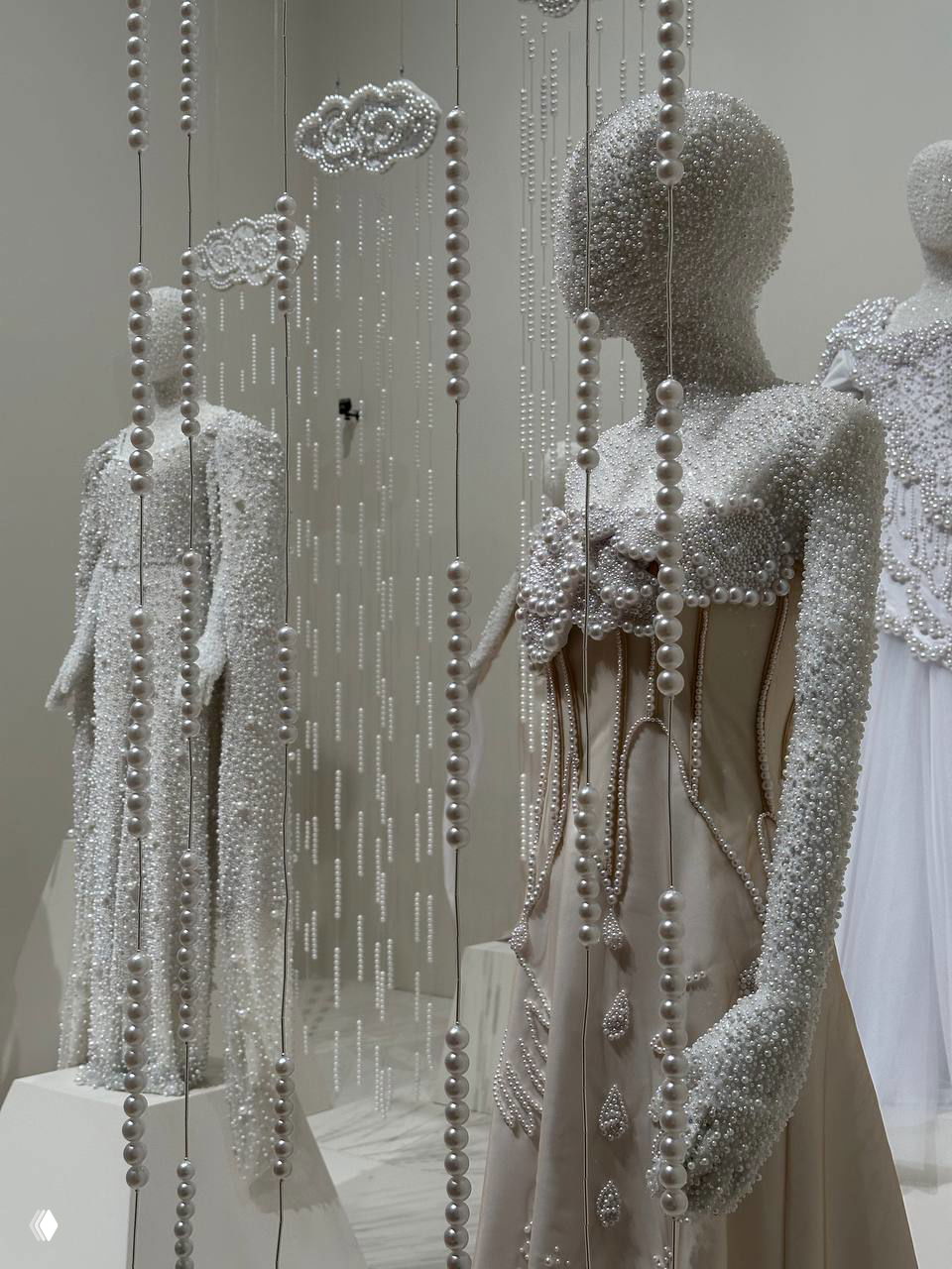 Две фигуры в декоративных платьях с перьевой фактурой и строгим силуэтом на нейтральном фоне — сочетание традиционных мотивов и современного дизайна.