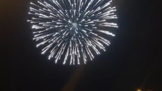 Крупный план фейерверка в ночном небе: белые и серебристые искры, яркие вспышки и силуэты зрителей внизу кадра на празднике.