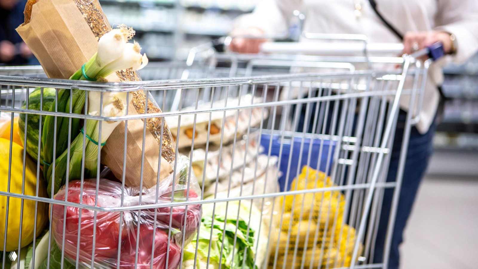 Тележка с продуктами в супермаркете — хлеб, овощи и упакованные товары, иллюстрация изменений цен на продукты в обзоре инфляции.
