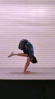 Тренер демонстрирует стойку на руках в прогрессивной вариации на сцене/в зале: тело согнуто, акцент на синхронизации плеч, запястий и корпуса.