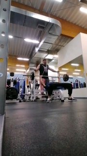 Атлет в спортзале выполняет жим лёжа на скамье под наблюдением тренера; кадр с пола подчёркивает контраст силовой закачки и работы над стойкой на руках.