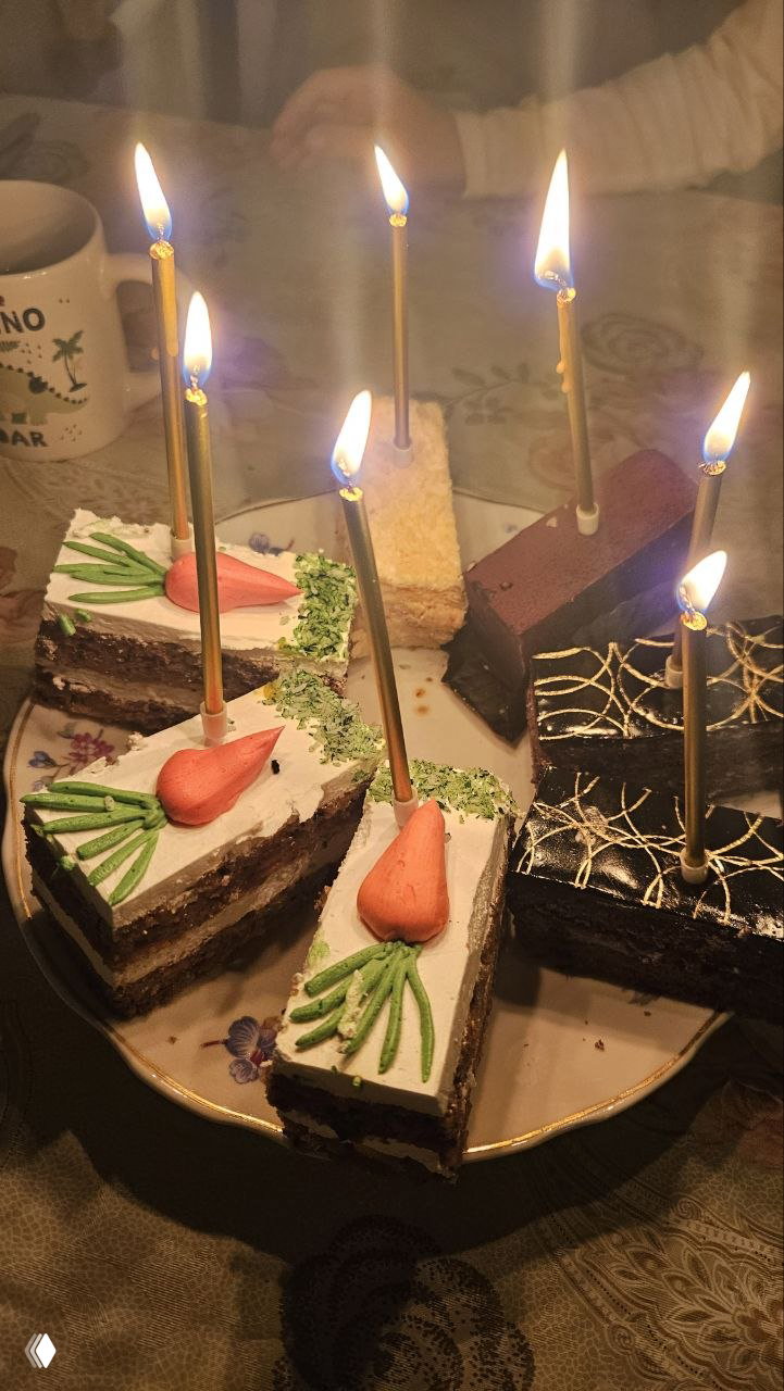 Порционные кусочки торта с зажжёнными свечами на тарелке, праздничная сервировка вечером во время дня рождения ребёнка.