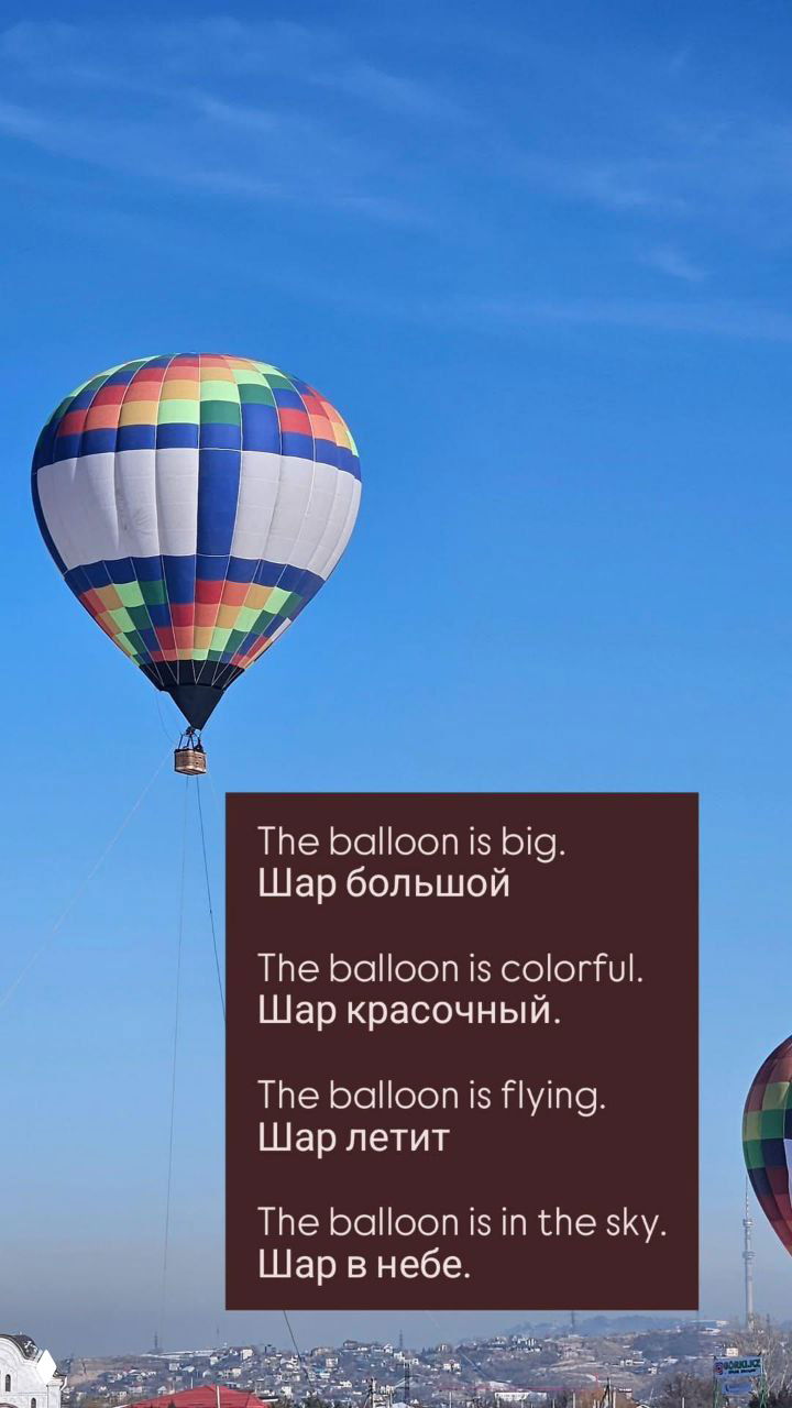 Крупный план одного разноцветного воздушного шара на фоне чистого голубого неба; внизу виден силуэт города и холмы.